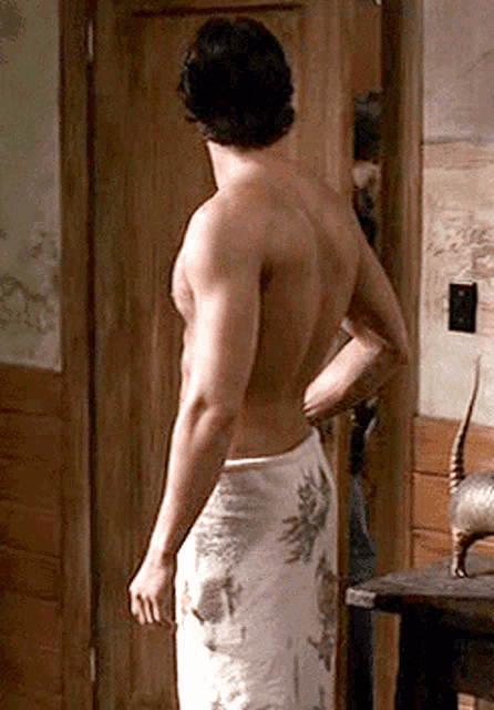 a shirtless man wrapped in a towel is standing in front of a door .