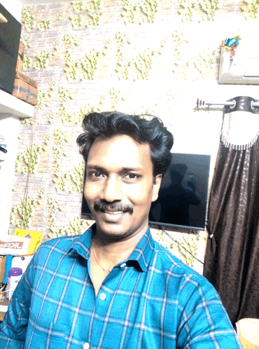 a man in a blue plaid shirt is taking a selfie in front of a tv