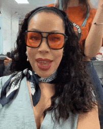 a woman wearing sunglasses and a scarf is smiling and wearing an orange headband