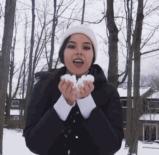 a woman wearing a white hat and a black jacket is holding snow in her hands