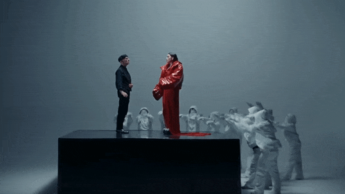 a man in a black suit stands next to a woman in a red coat on a stage