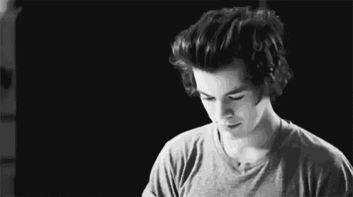 a black and white photo of a young man with curly hair wearing a gray shirt .