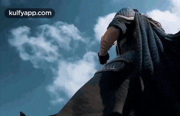 a man in a cape is riding a horse in front of a cloudy sky .