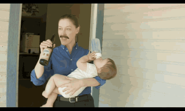 a woman with a mustache is holding a baby and drinking from a bottle with a label that says lion
