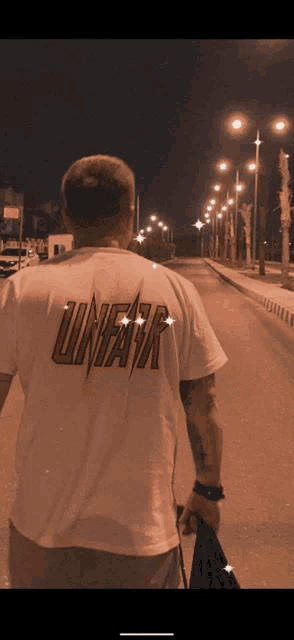 a man wearing a white shirt with the word linear on the back is walking down a street at night