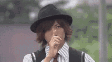 a man wearing a hat and striped shirt is holding his finger to his mouth .
