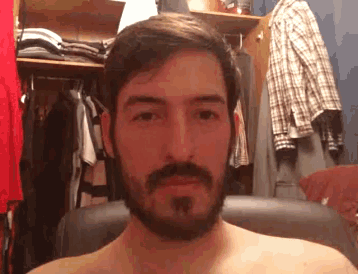 a shirtless man with a beard is sitting in front of a closet full of clothes