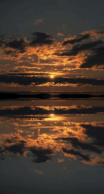 a sunset over a body of water with clouds reflected in it