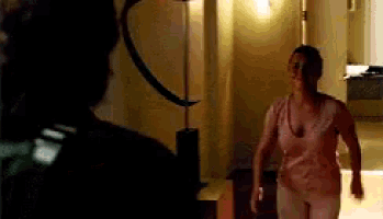 a woman in a pink tank top is walking in a dark room