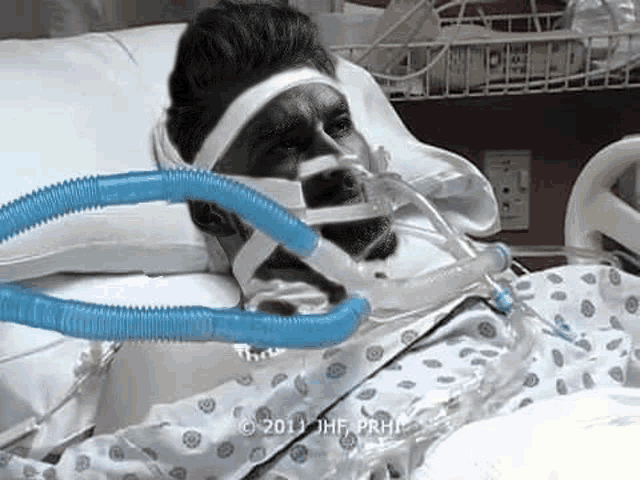 a man is laying in a hospital bed with an oxygen mask on his head .