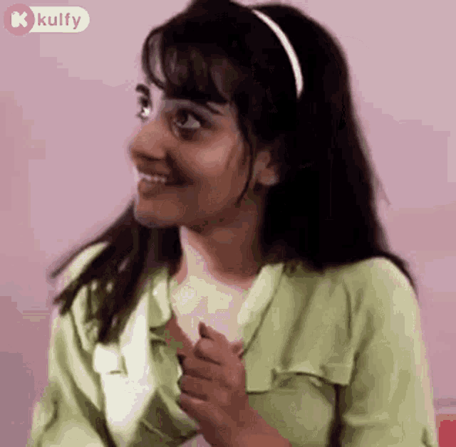 a woman wearing a green shirt and a headband is smiling and looking to the side .