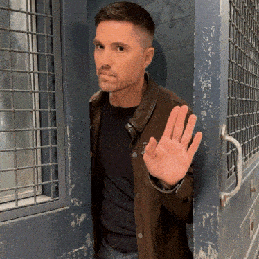 a man in a brown jacket holds up his hand in front of a door