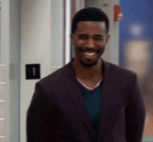 a man in a suit is smiling in front of a door with a number 1 on it .