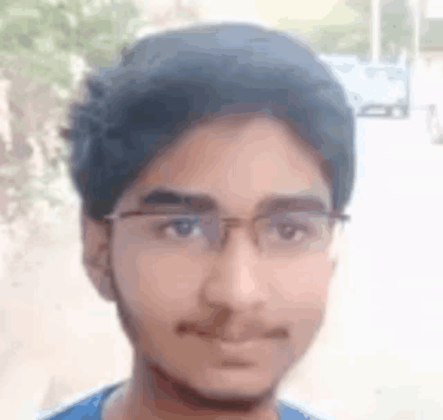 a young man wearing glasses and a blue shirt is looking at the camera and smiling .
