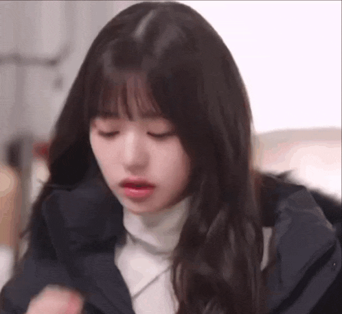 a close up of a girl with long hair and bangs wearing a black jacket and a white turtleneck .