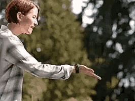 a woman in a plaid shirt is reaching out her hand towards a tree .