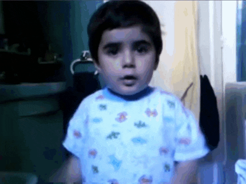 a young boy wearing a blue shirt with the letter a on it looks at the camera