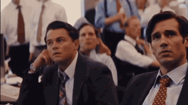 a group of men in suits and ties are sitting in a classroom looking at a computer screen .