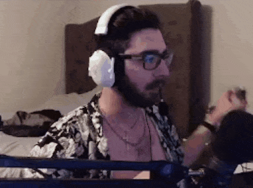 a man wearing headphones and glasses is sitting in front of a microphone in a bedroom .