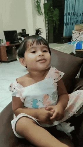 a little girl is sitting on a couch making a funny face .