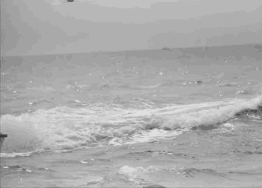 a black and white photo of a dolphin jumping out of the water in the ocean .