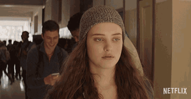 a girl wearing a knitted hat is standing in a hallway with netflix written on the bottom