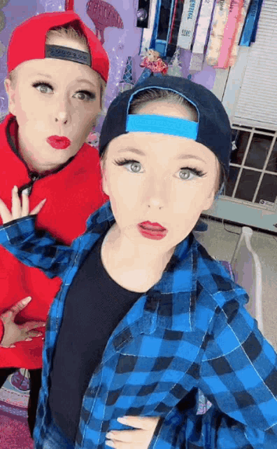 a girl wearing a blue plaid shirt stands next to another girl wearing a red sweater