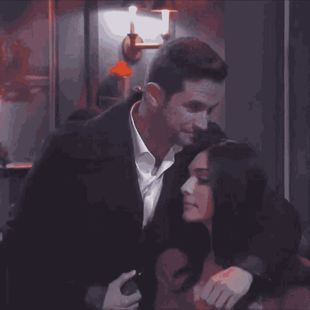 a man in a suit is hugging a woman in a red top