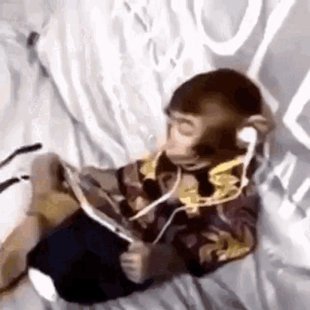 a monkey is sitting on a bed wearing headphones and a tablet .