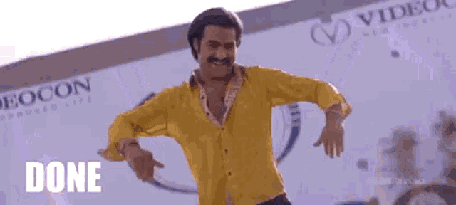 a man in a yellow shirt is dancing in front of a building and the word done is on the screen .