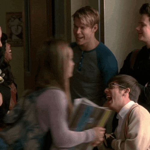 a group of people are standing in a hallway and one of them is wearing glasses and holding a magazine