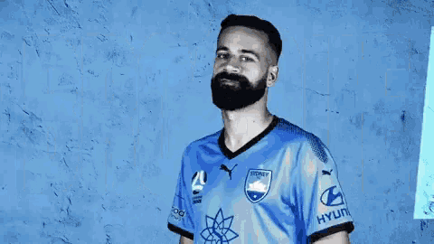 a man with a beard is wearing a blue soccer jersey with hyundai on the sleeves .