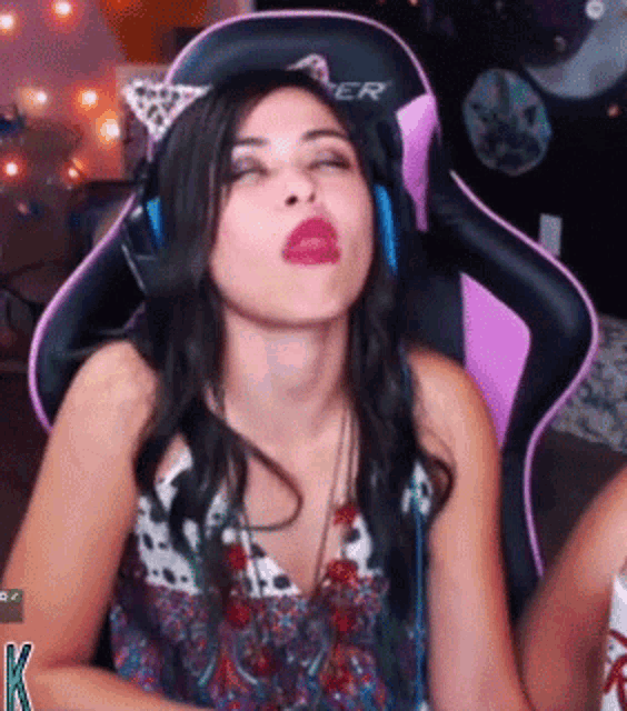 a woman wearing headphones and a cat ear headband is sitting in a pink and black gaming chair .