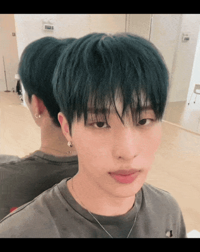 a young man with green hair looks at the camera in front of a mirror