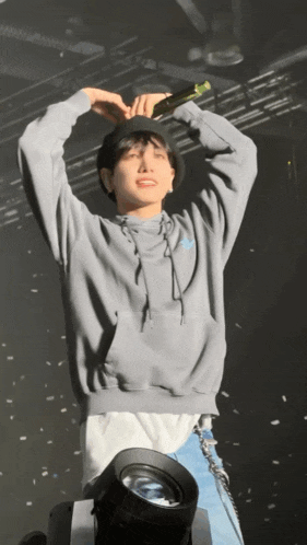 a young man wearing a grey hoodie is holding a microphone