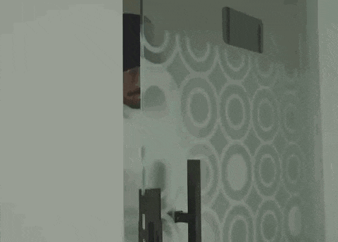 a man is peeking out from behind a glass door in a room .