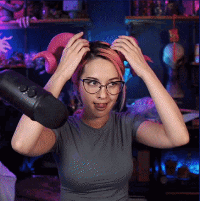 a woman wearing glasses and a headband adjusts her hair while standing in front of a microphone