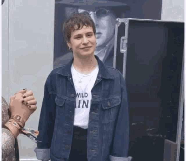 a woman in a denim jacket is wearing a white shirt that says wild in