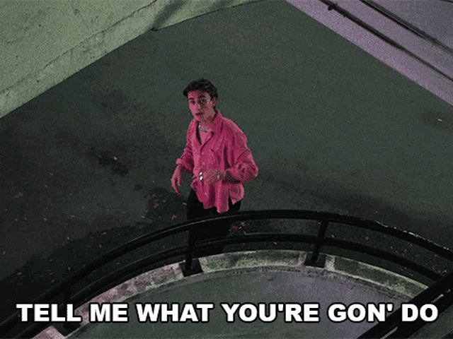 a man in a pink shirt is standing on a set of stairs with the words tell me what you 're gon ' do
