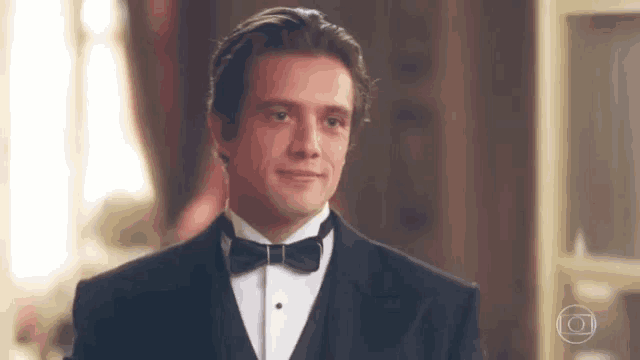 a man wearing a tuxedo and bow tie is smiling .