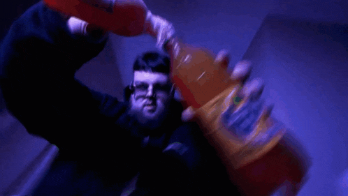 a man in a black jacket is holding a green bottle of soda