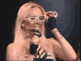 a woman wearing glasses and headphones is holding a microphone and adjusting her glasses .