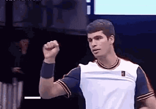 a tennis player is raising his fist in the air while wearing a white shirt .