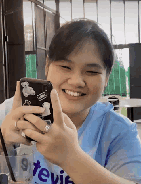a woman wearing a blue tevin shirt smiles while holding a phone