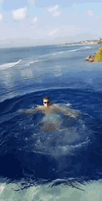 a man is swimming in a pool with the ocean behind him