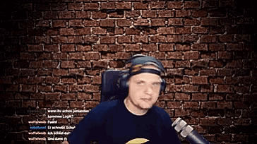 a man wearing headphones is sitting in front of a brick wall and a microphone
