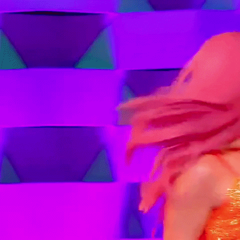 a drag queen with pink hair is standing in front of a purple wall with lights .