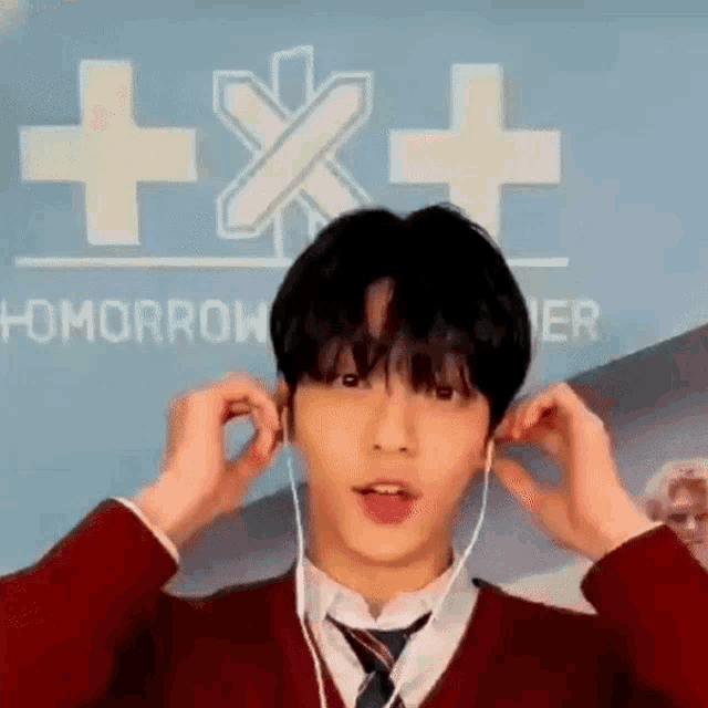 a young man wearing a red sweater and tie is putting on earphones .