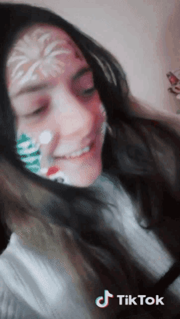 a girl with a christmas tree painted on her face has a tiktok watermark on the bottom right