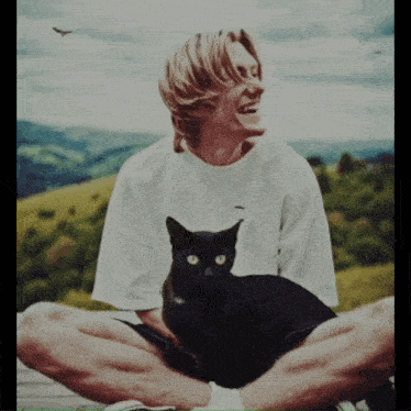 a man in a white shirt is sitting with his legs crossed and a black cat on his lap